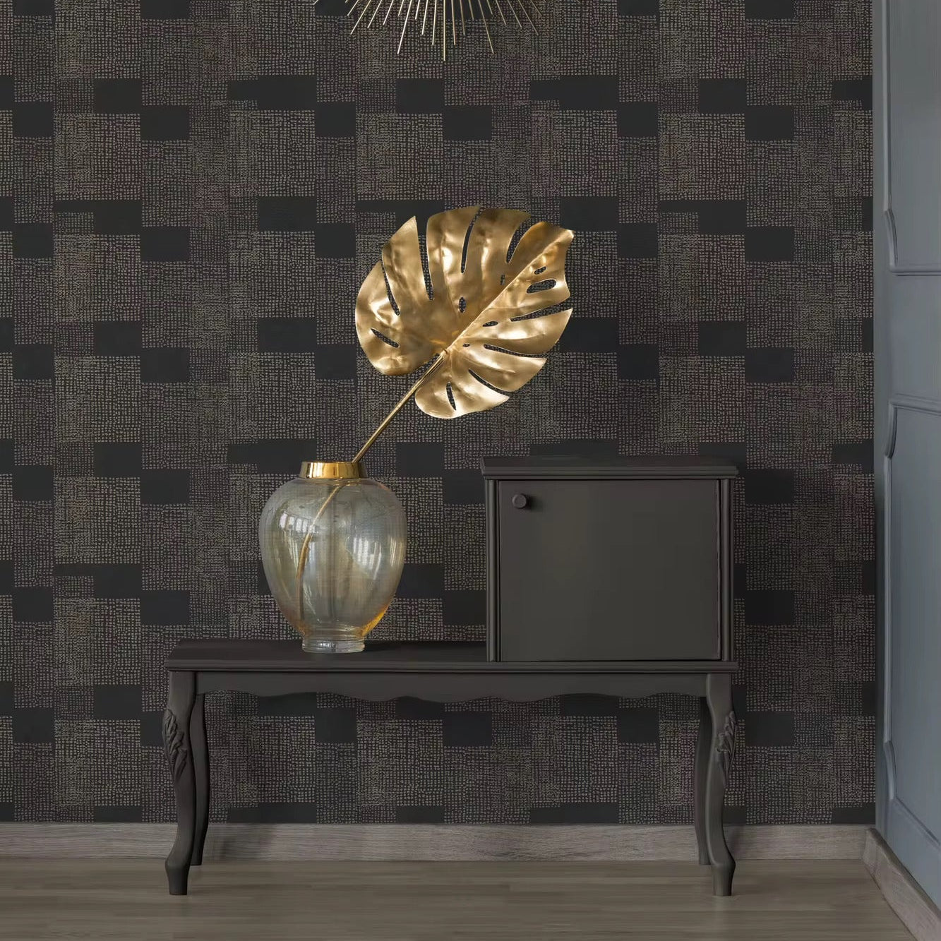 Decorative interior setting with a gold leaf sculpture, vase, and mirror on a dark patterned wall.
