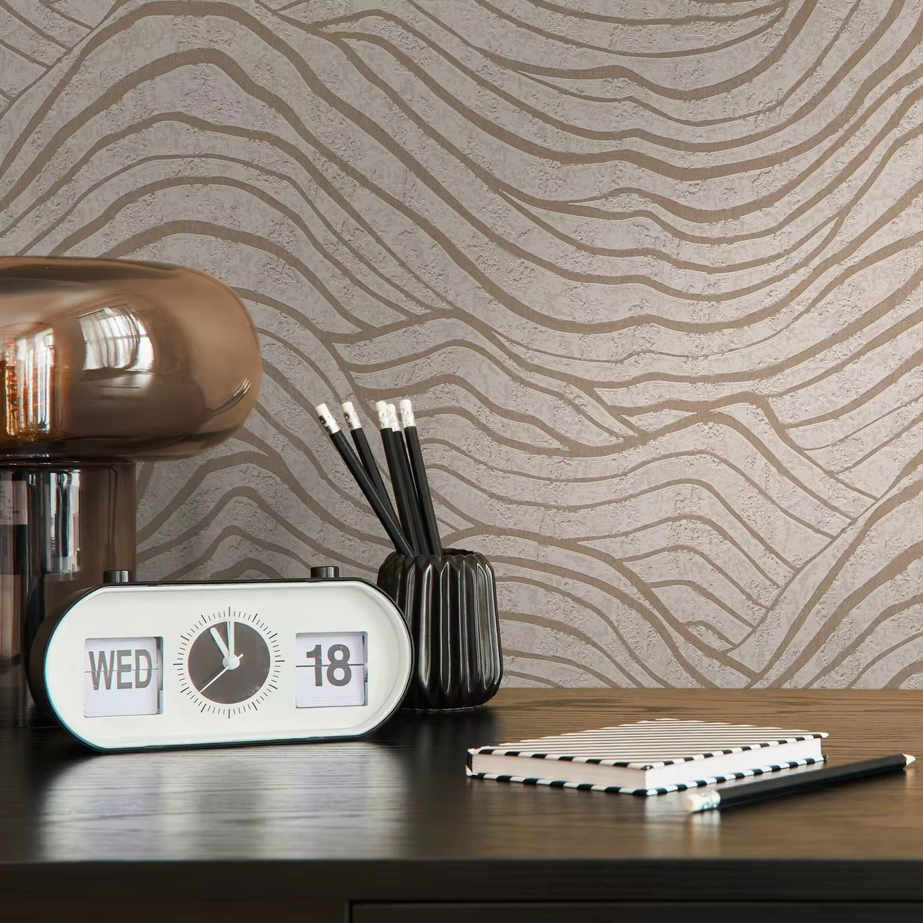 Desk setup with a clock, pen holder, and notebook against a wavy patterned wallpaper