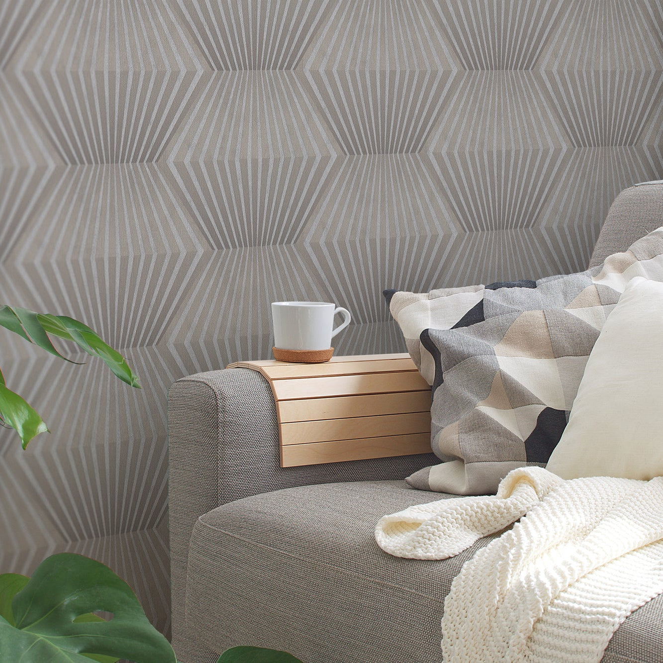 Gray geometric patterned wallpaper  with a gray sofa, wooden side table, and white mug.